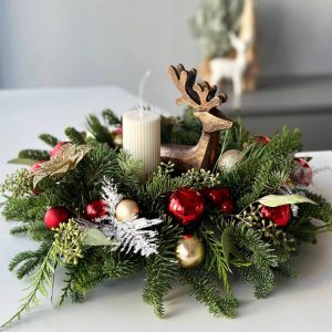 Crimson Elegance: Table centerpiece with an elegant reindeer and vibrant red New Year's wreath adorned with festive ornaments. Perfect for adding warmth and sophistication to your holiday table setting.